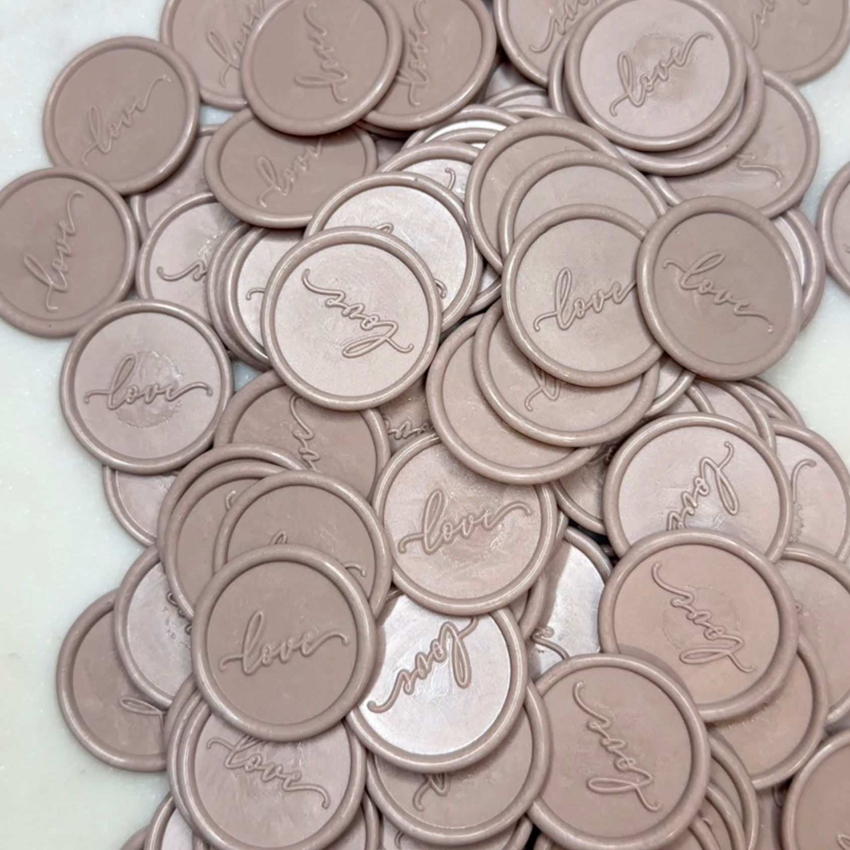 A pile of wax seal with the word love pressed on them in a dusty rose colour