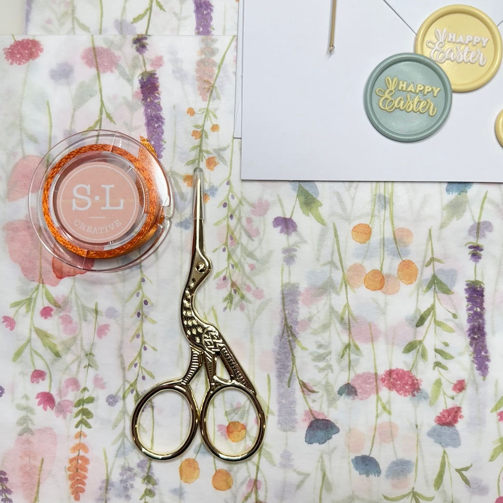 Thumbnail: burnt orange ribbon in spool with crane scissors and wax seals on envelope on top of floral tissue paper