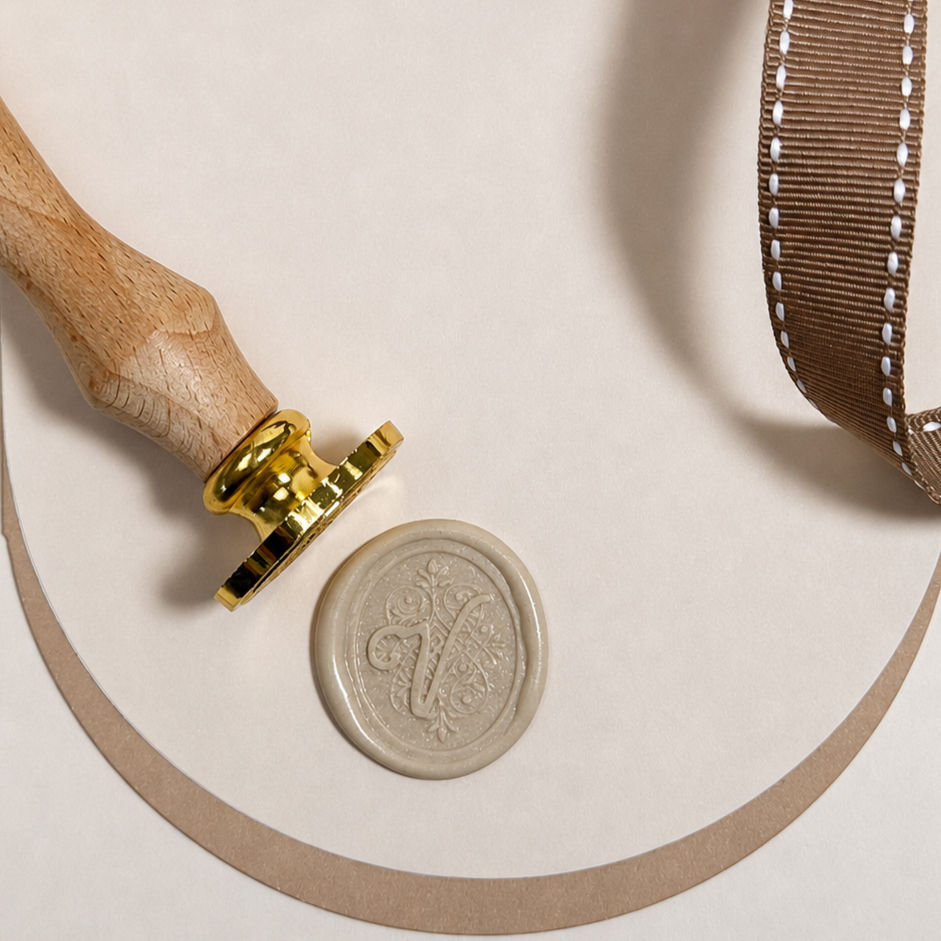 Thumbnail: Close up of Wax Seal & Stamp with the Letter V in Cursive Script on Curved Background with a Ribbon to the side