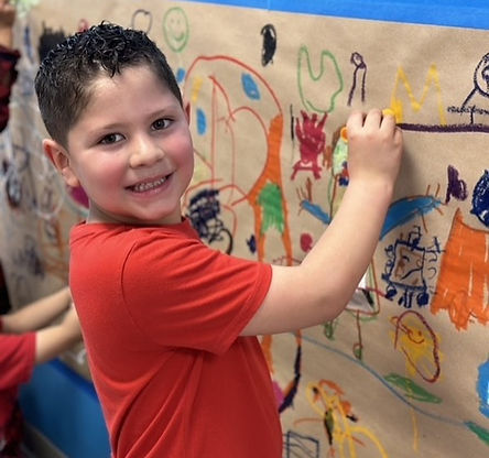 A pre-k boy drawing on paper on a wall.