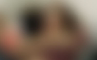 Duas pessoas se abraçando calorosamente; uma mulher visível com expressão emocional e olhos fechados enquanto recebe o abraço, em um ambiente interno com outras pessoas desfocadas ao fundo.