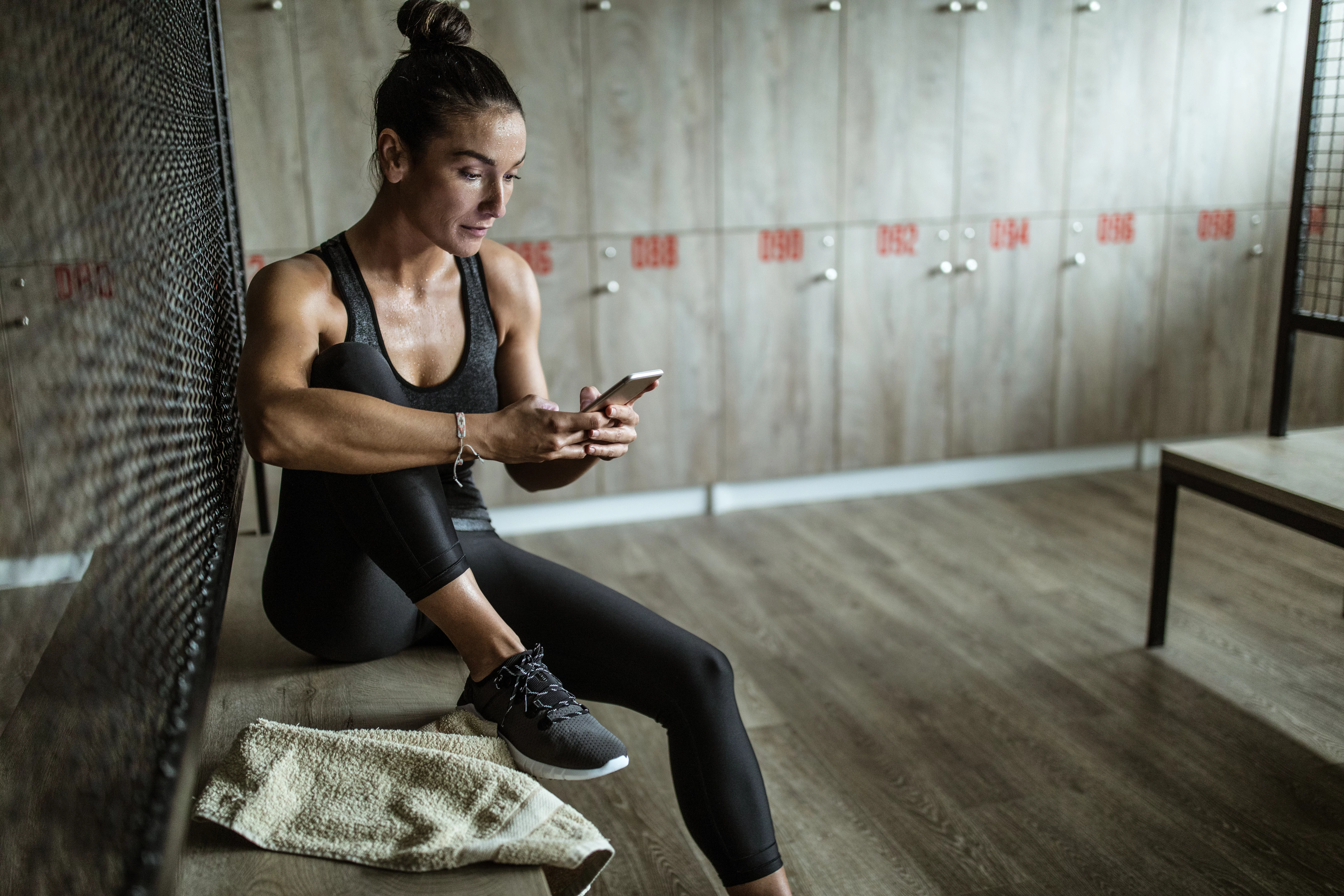 Femme en forme assise dans le vestiaire au gym regarde son téléphone.