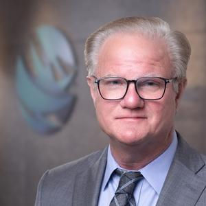 Professional headshot of a man with glasses and grey suit