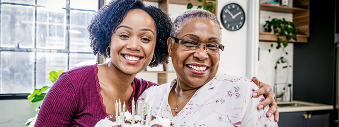 Two women smiling with a birthday cake in a kitchen.