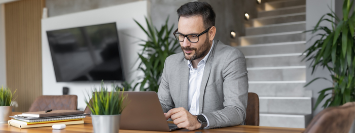 Man in a grey suit working on a laptop in a modern office