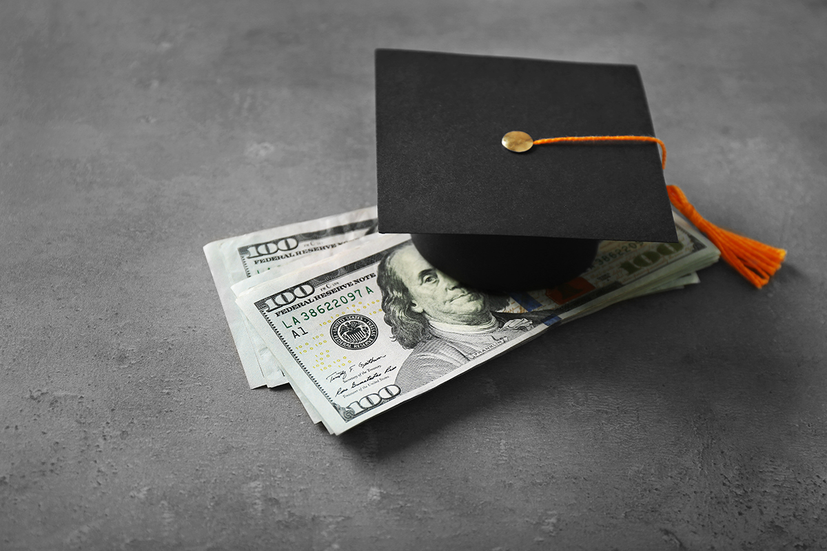Small graduation cap resting on a stack of hundred dollar bills