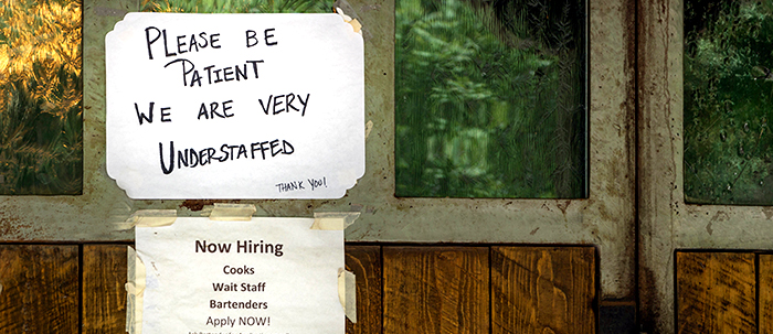 Handwritten understaffed sign and Now Hiring notice on a window