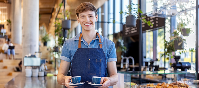 Smiling barista holding two cups of coffee in a bright cafe