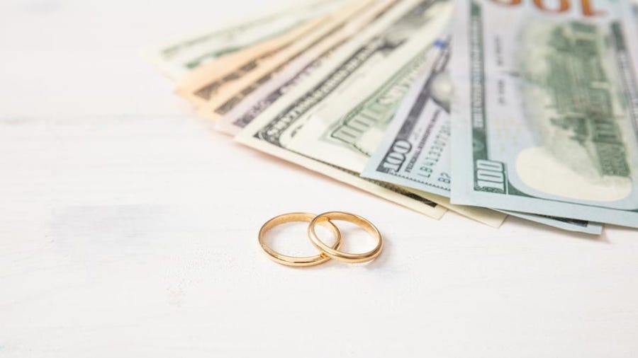 Two gold wedding rings next to a fan of US dollar bills.