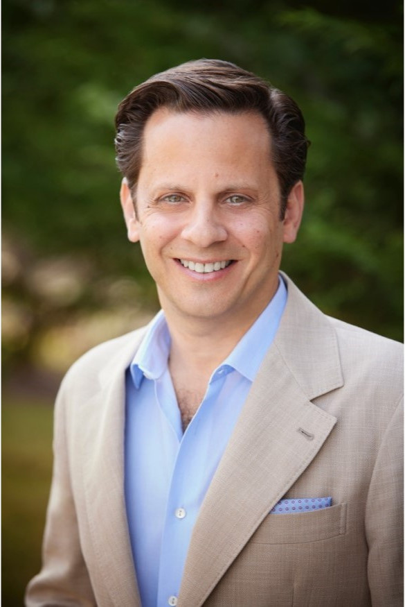Smiling man in a tan blazer and light blue shirt