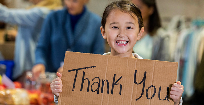 Smiling young girl holding a cardboard Thank You sign.