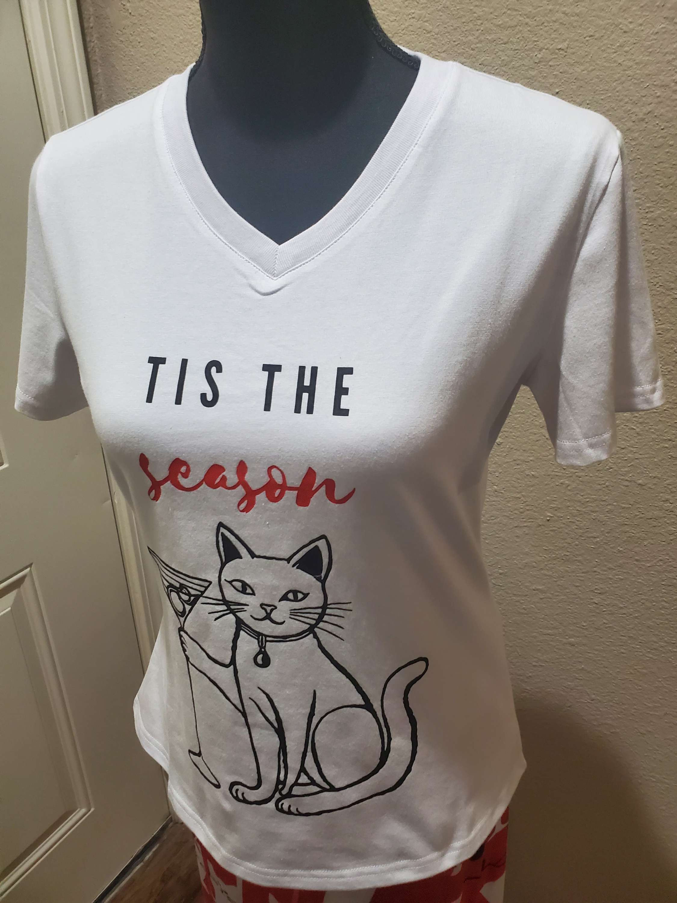 Mannequin with a white t-shirt with a minimalist illustration of a cat holding a martini and the slogan "Tis The Season"