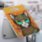 Colorful cat illustration with sunglasses on a luggage tag, attached to a silver suitcase and a blurred outdoor background.