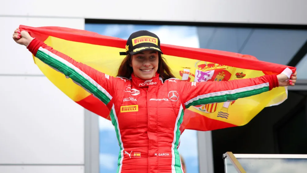 Driver Marta García holds a Spanish flag and celebrates her first win in F1 Academy
