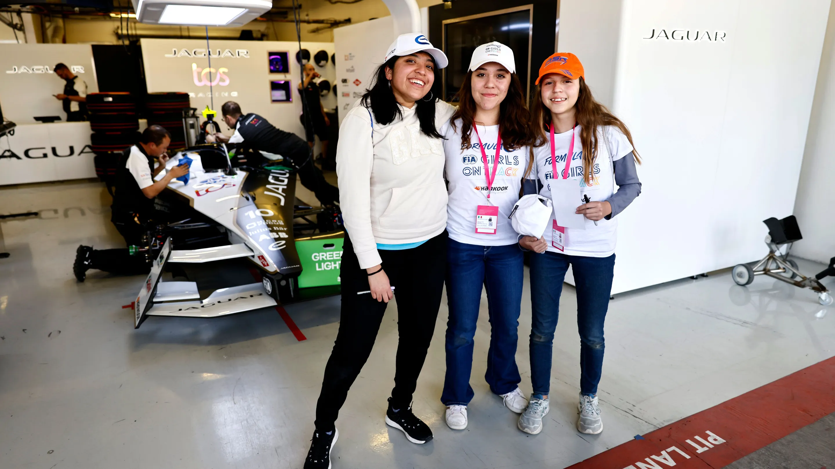 A Mexican woman and two Mexican girls smiling in front of a Formula E car