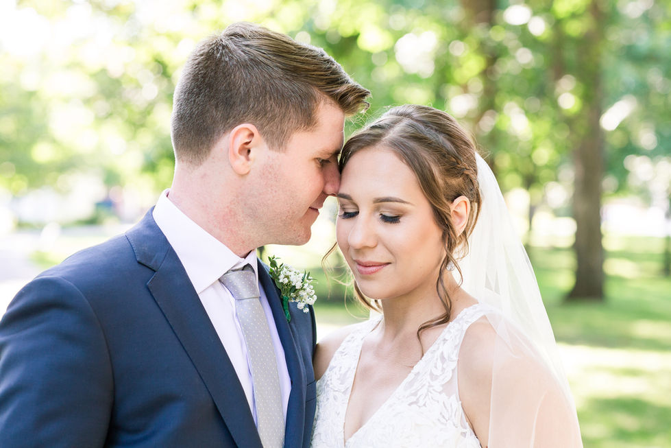 Bride and groom embracing outdoors, eyes closed.