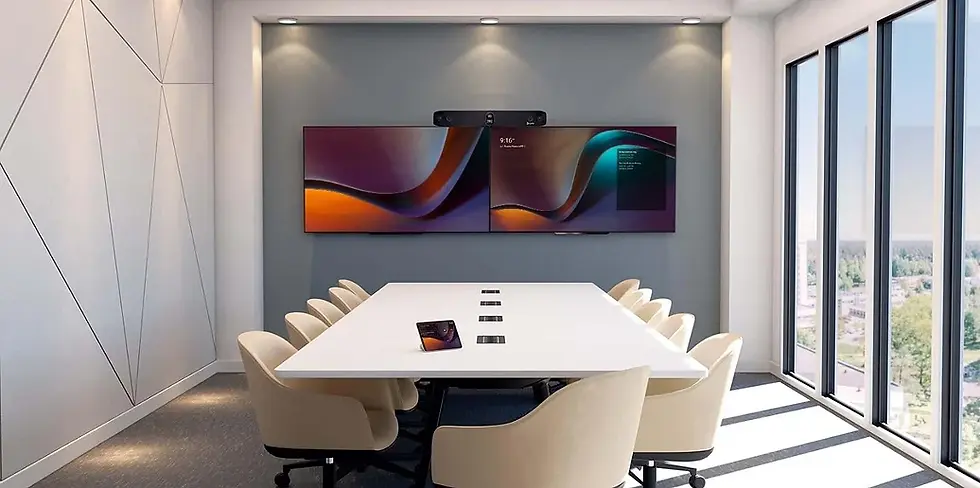 Modern conference room with a long white table, beige chairs, dual screens displaying abstract art. Bright windows on the right side.