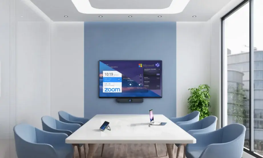 Modern conference room with a screen showing Zoom and Microsoft apps. Blue chairs surround a white table, with a phone on it. Bright and minimal.