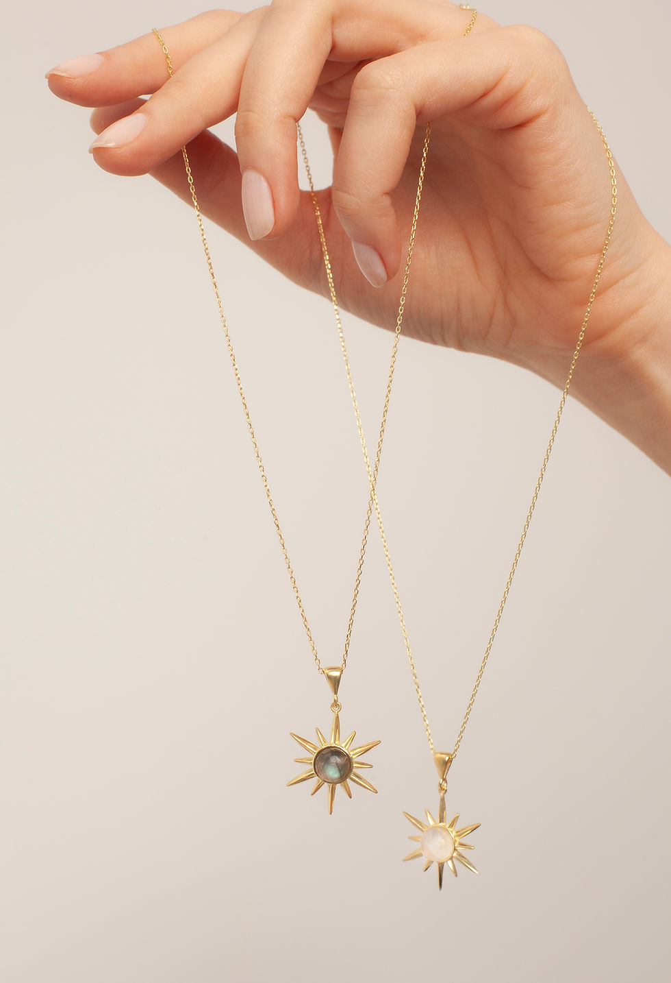 Hand holding two gold sun necklaces