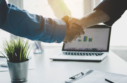 Two individuals shaking hands over a laptop, symbolizing a business agreement or collaboration.