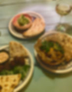 Three plates of food and a glass of white wine on bench at hamsa restaurant in Krakow, in summer