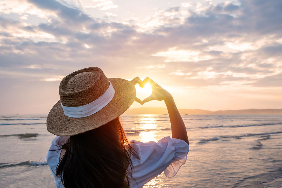 Young woman traveler making heart shape with hands and looking beautiful sunset on the bea