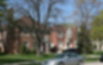 A row of houses with front yards and trees, and some cars parked in front of them