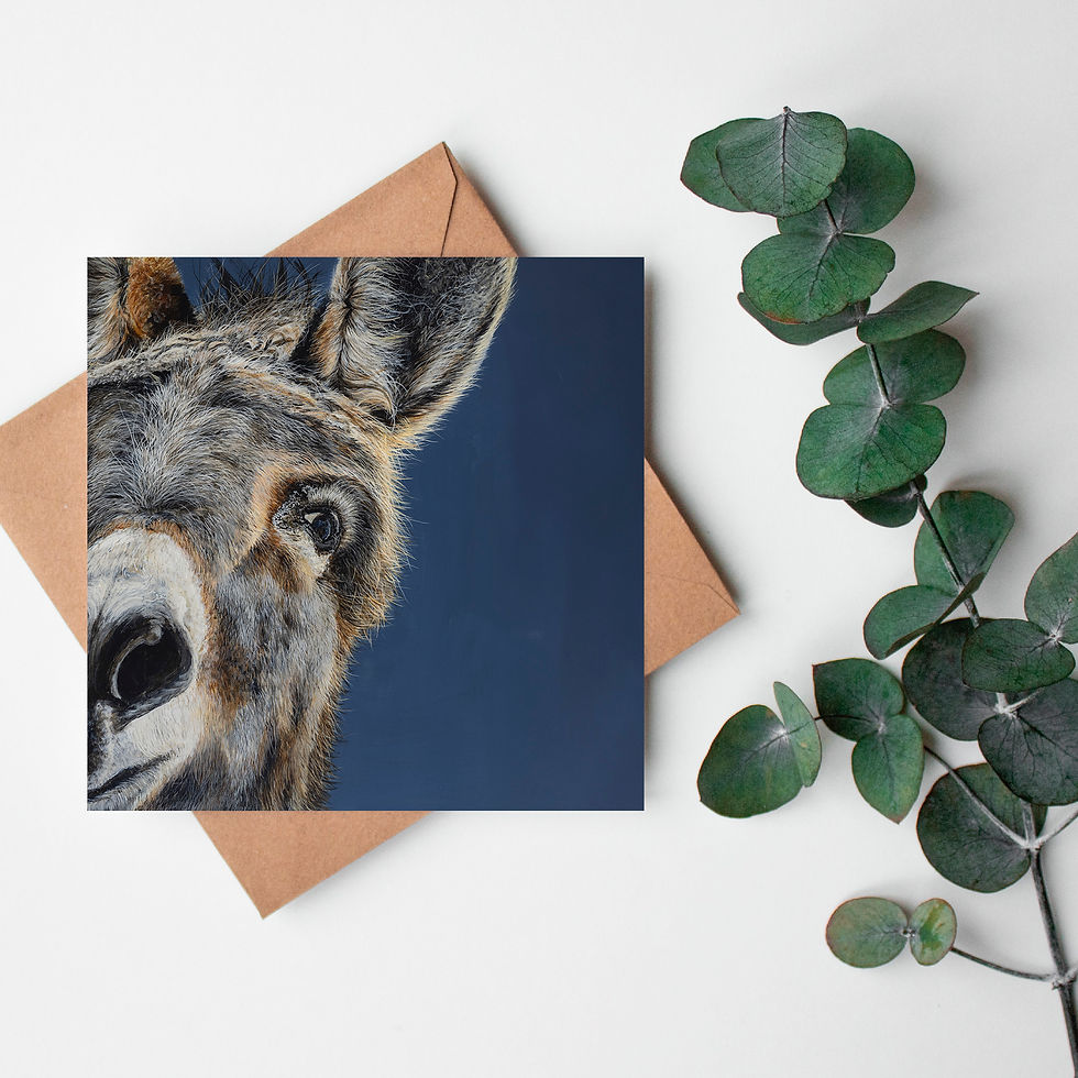 A greeting card of the face of a donkey. It is lying flat across a kraft brown envelope placed beside a sprig of eucalyptus