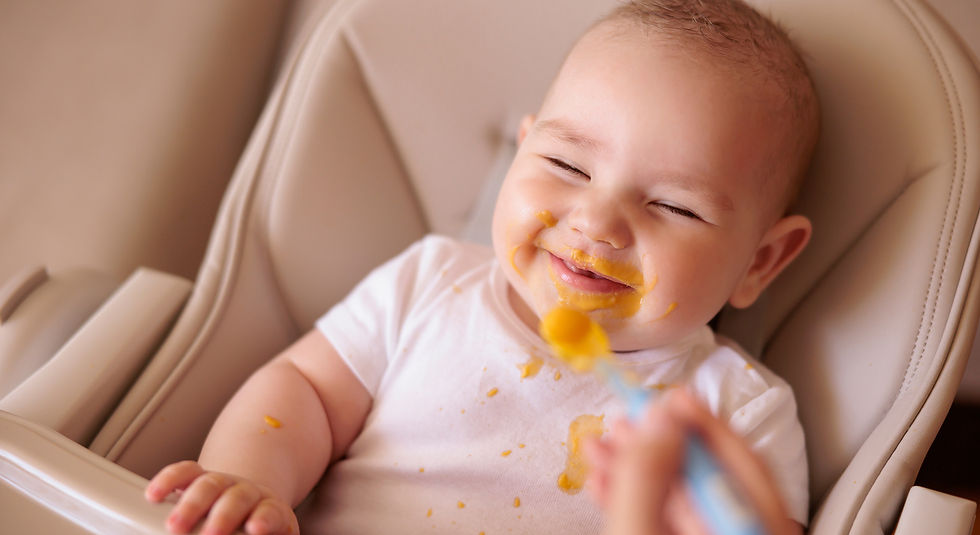 Smiling baby in high chair, face messy with orange baby food, wearing a white shirt, creating a playful and joyful mood.