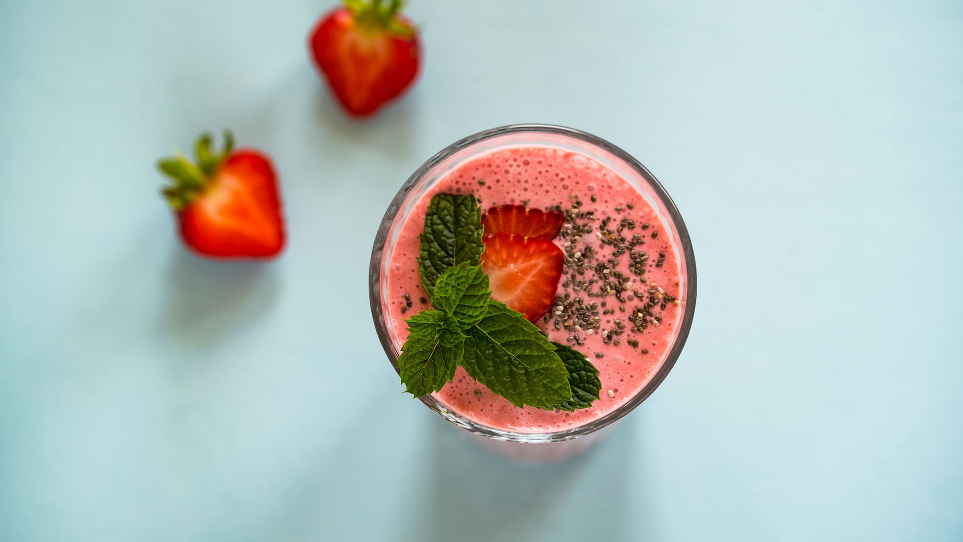 A strawberry smoothie in a glass topped with basil, fresh strawberry slices and chia seeds