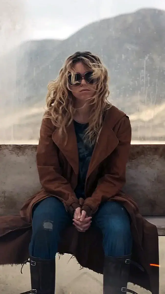 Milly Alcock as Supergirl sitting in a worn brown coat.