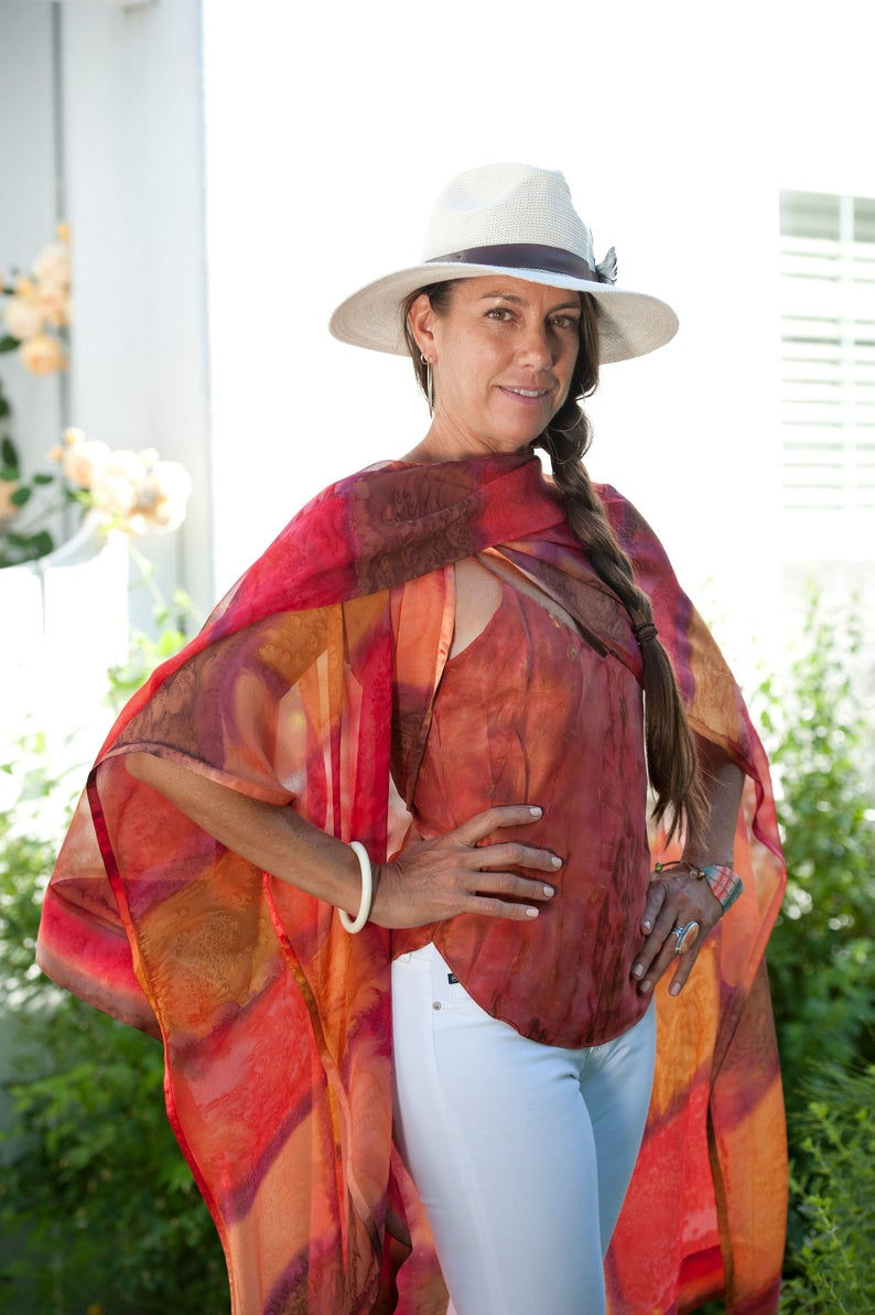 Thumbnail: Side view of woman wearing silk ruana Sunset toned stained glass pattern of vibrant hues of tangerine, sienna and poppy red