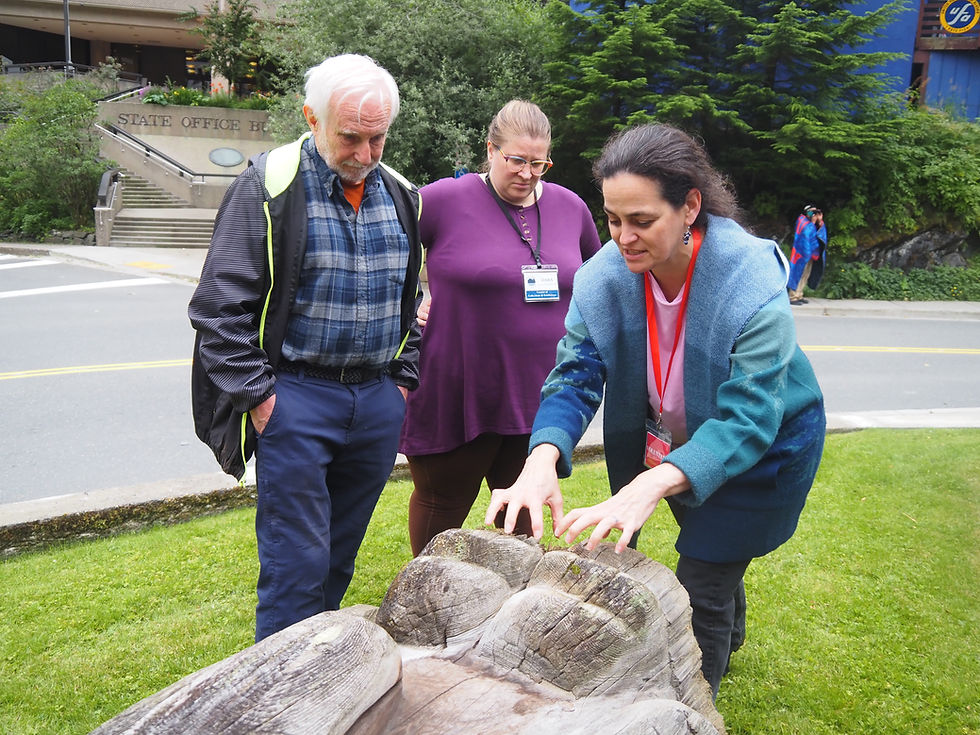 Ellen Carrlee, Dara Lohnes-Davies and Ray Watkins discuss the dry rot on the inside of the base of the Harnessing of the Atom totem pole on July 23, 2025. (Natalie Buttner / Juneau Independent)