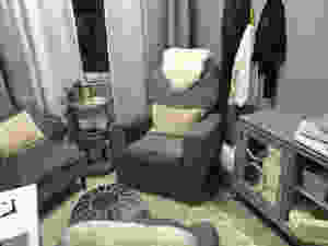 A pai of soft grey chairs sit either side of a silver table holding a book and a plant. There is a credenza to the right with an infant scale on top and mirrored doors. An ottoman sits in the cnter of the room and another grey office chair with a soft pillow is facing the original two chairs.