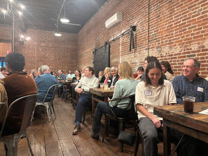 People of all ages sitting together at coffee shop tables, smiling and laughing and engaging in conversation. Community gathering to build connections