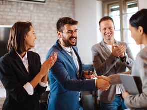 Man shaking hands with woman and people either side congratulating