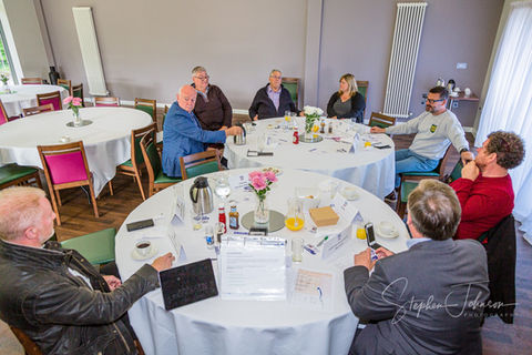 Business meeting: colleagues gather around tables for breakfast, engaging in discussion.
