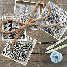 An image of 4 tangled art tiles, with a twine string tied into a bow sitting on top. There are traditional tangle pens on the table.