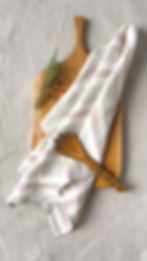 Essuie-vaisselle en lin lavé délicatement disposé sur une planche en bois, accompagné de herbes aromatiques et d'une cuillère