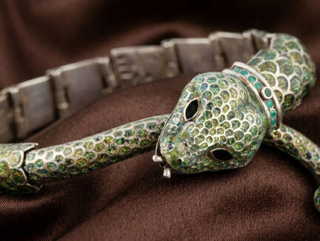 Pulsera en forma de serpiente con incrustaciones verdes y turquesa sobre tela marrón.