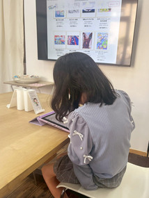 テーブルでタブレットを使う少女、背景に大きな画面