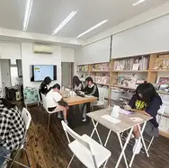 机に向かって制作する子どもたちと、本棚のある教室の内観