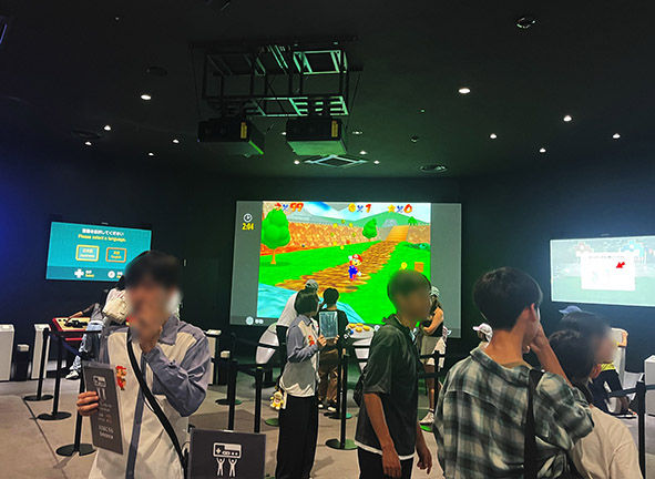 ニンテンドーミュージアム内で、巨大なスクリーンに映し出されたスーパーマリオのゲームを体験する来場者たち