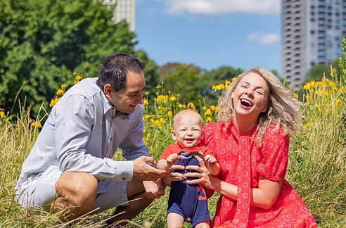 man and woman holding baby while sitting in the grass at Lincoln Park chicago family portrait photographer in chicago chicago family photographer photographed by pamela l king photography