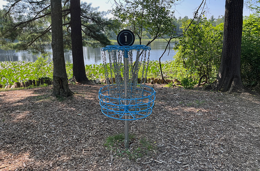 Blue disc golf basket near the lake at Punderson State Park surrounded by trees and water views.