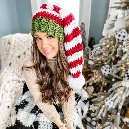 Smiling woman wearing a festive red, white, and green crochet elf hat, made from an Elf crochet pattern.