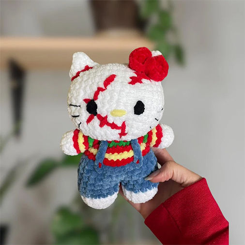 Hello Kitty Chucky crochet doll in blue overalls with red bow, handmade amigurumi figure being held outdoors