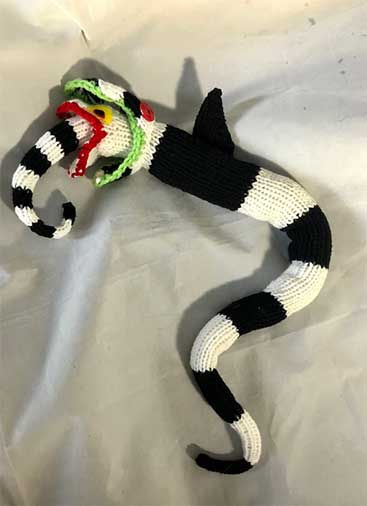 A Beetlejuice knitting pattern for a mug cozy made with bright green, black and white yarn.