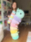 Woman holding large pastel crochet caterpillar plush with segmented body and round head indoors.