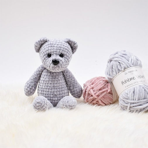 Teddy bear crochet pattern made with soft gray velvet yarn, sitting next to skeins of pink and gray yarn, designed in a cute and simple style.